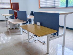 Contuo office showroom displaying 12+ height-adjustable desk models with ergonomic frames, cable management systems, and modular privacy panels in modern workspace setting.